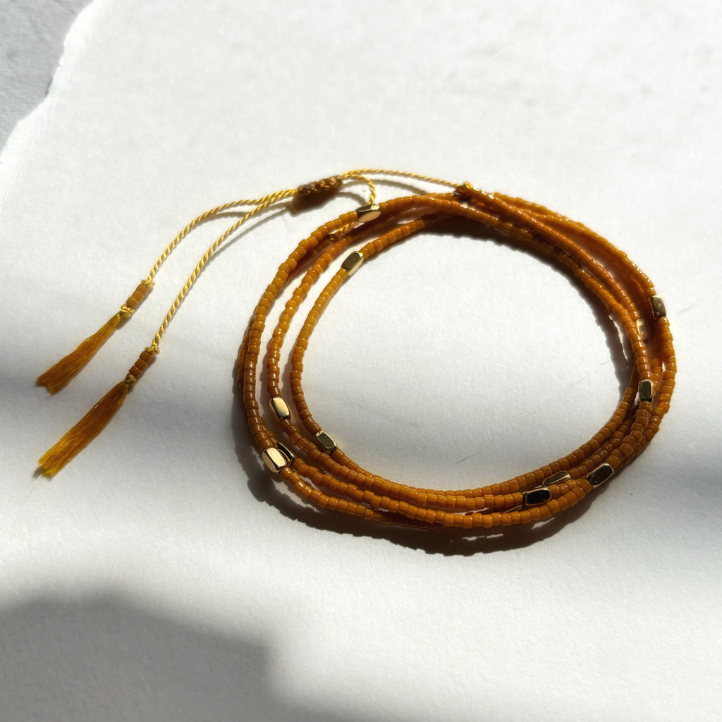 Bracelet wrap miyuki ocre Marlah posé sur papier blanc