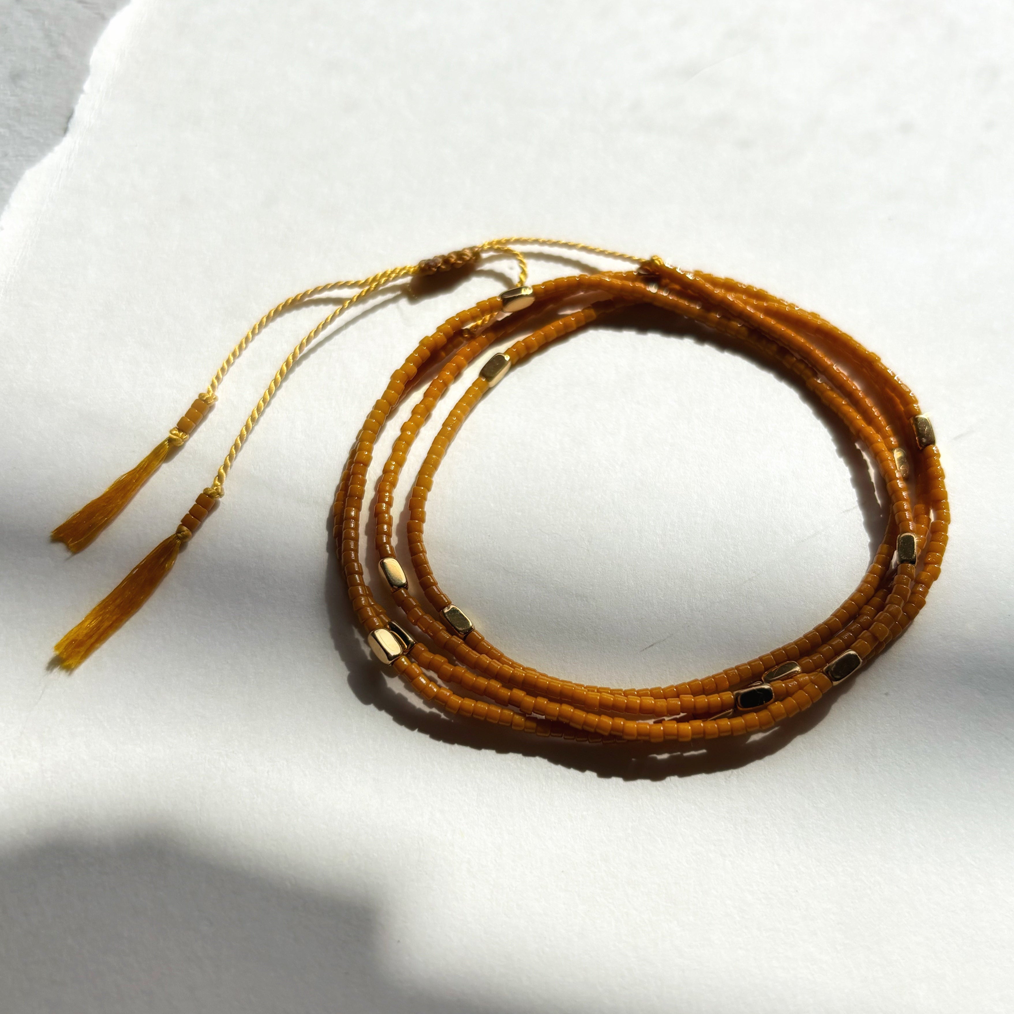 Bracelet wrap miyuki ocre Marlah posé sur papier blanc