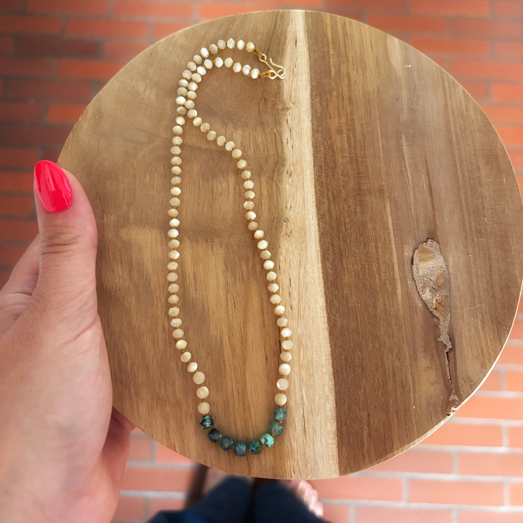 collier nacre et turquoise posé sur un plateau rond en bois