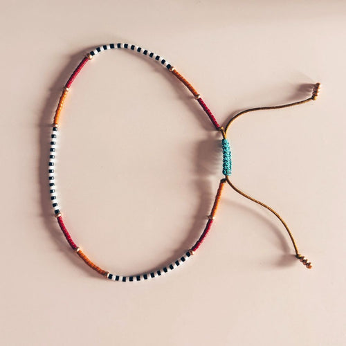 Bracelet de cheville Ibiza MarlaH coloris noir, blanc, ocre et rouge en perles Miyuki avec cordon ocre à nœud coulissant