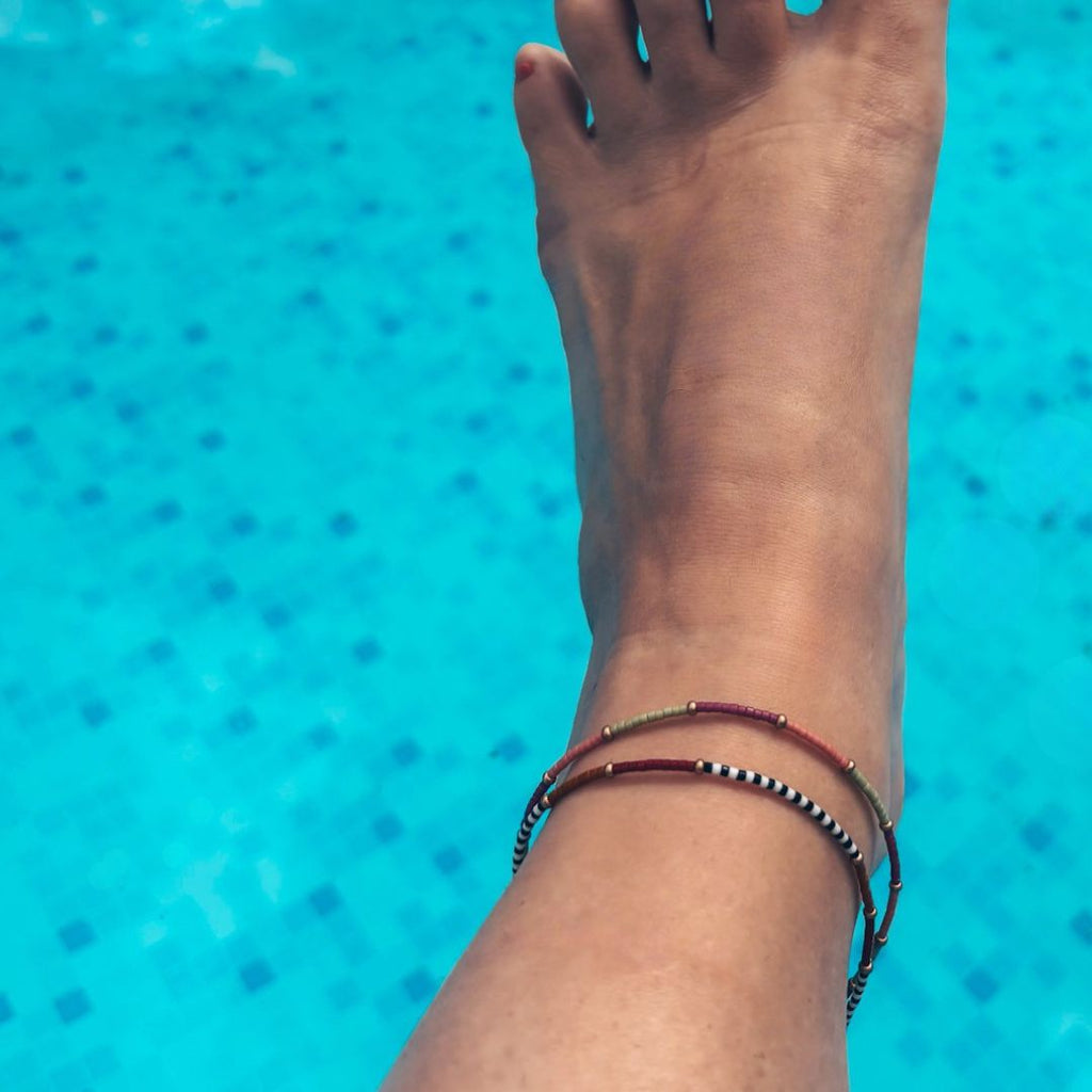 Bracelets de cheville Ibiza MarlaH portés à la cheville au bord d'une piscine, perles Miyuki et cordon ocre, ambiance festival