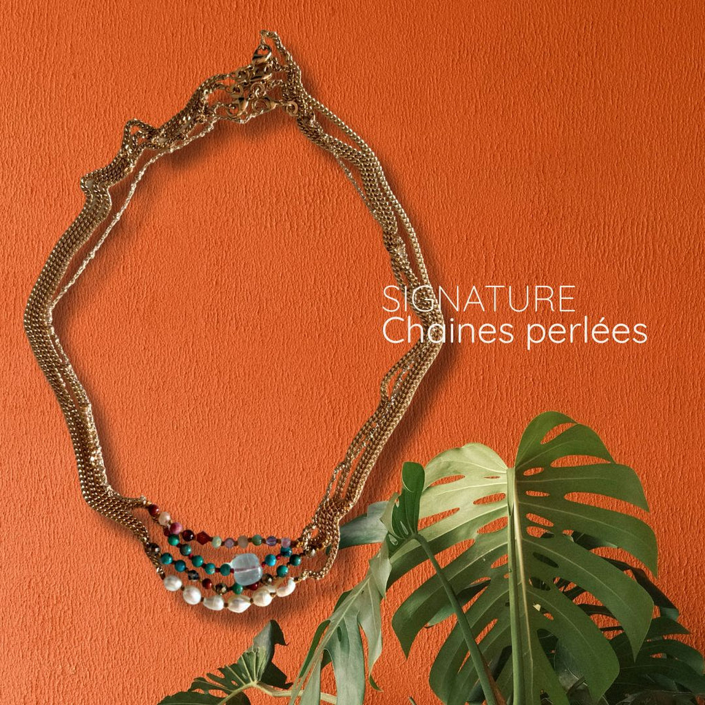 Collier chaîne perlée Signature plaqué or 750 posé sur fond orange avec une plante