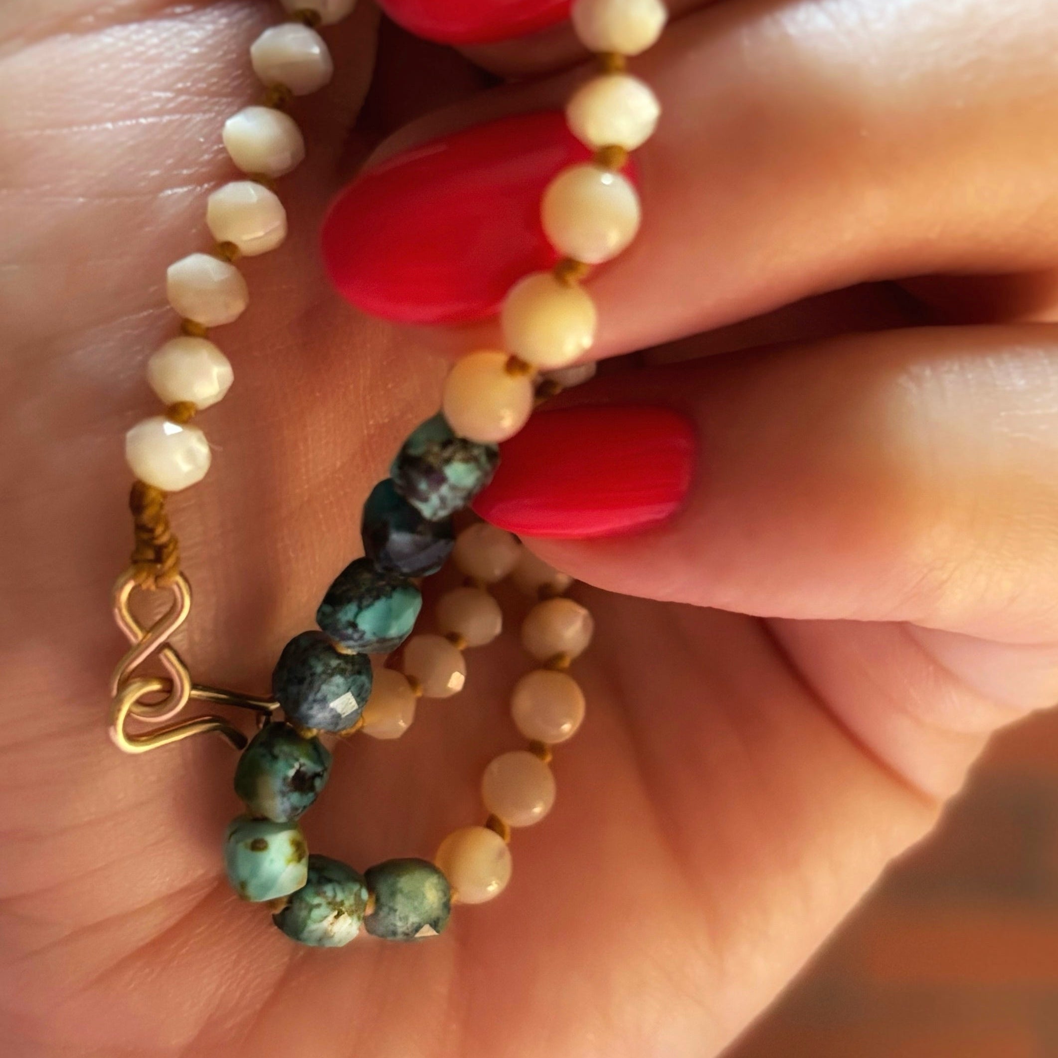 Gros plan sur le fermoir gold filled du collier Signature, perles de nacre et turquoise naturelle tenues à la main