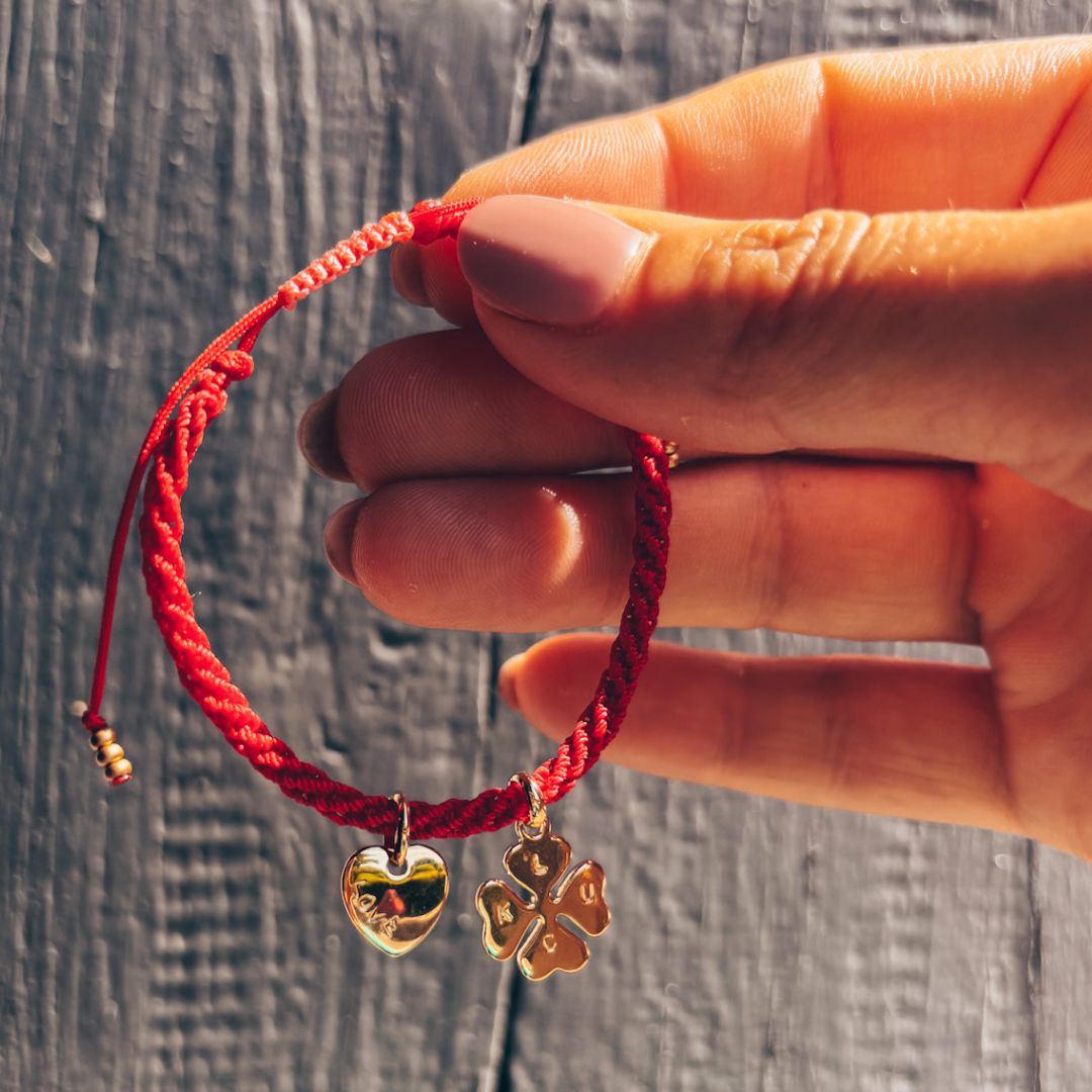 Bracelet Talisman Lucky Love rouge tenu en main, nœud coulissant réglable rose corail