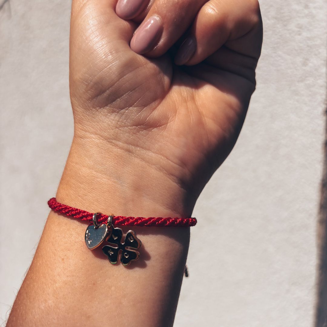 Bracelet Talisman Lucky Love rouge porté au poignet, breloques cœur et trèfle plaqué or